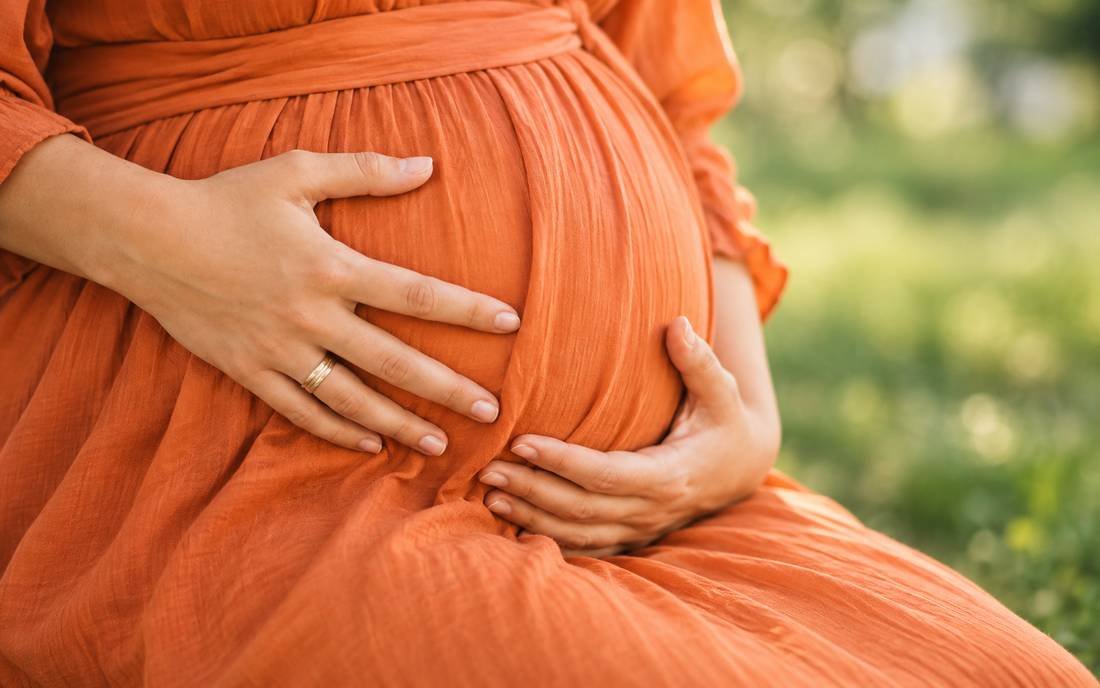 A close-up of a pregnant person's belly, hands resting gently on it